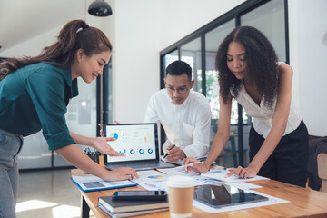 Collaborative Strategy: A diverse team of professionals huddle around a laptop, analyzing data and charts in a modern office setting. They are engaged in a collaborative discussion.
