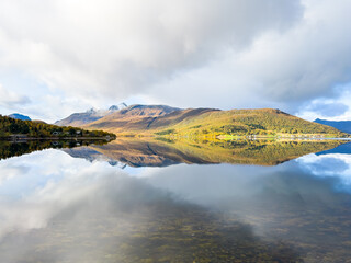 Autumn landscape of Senja Island, Northern Norway, with colorful trees, serene water reflections, and dramatic mountains.