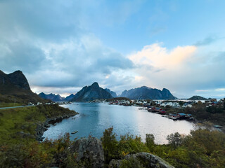 Autumn sunset in Reine, Lofoten Islands, Norway, with dramatic mountains, calm waters, and traditional houses along the shore.