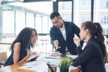 Focused Business Team Meeting: A diverse team of professionals collaborates intensely around a table, immersed in a serious discussion over documents and charts.