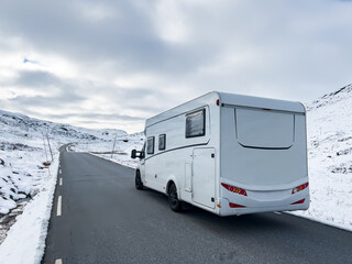 A motorhome driving along the Sognefjellsvegen road in Norway, surrounded by snow-covered mountains...