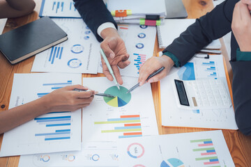 Business Strategy Meeting:  A diverse team of business professionals collaborate, analyzing charts and graphs around a wooden table.