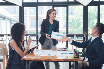 Collaborative Business Meeting:  A diverse team of professionals engages in a productive meeting, exchanging ideas and documents in a modern office setting.