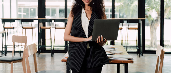 Businesswoman Working on Laptop in Cafe: A professional woman confidently works on her laptop, showcasing a modern and stylish business atmosphere in a trendy cafe setting.