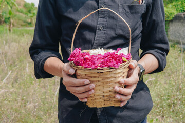 Indonesian man is holding a basket filled with mixed pink, red, and white flowers.
