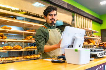 Fototapeta premium Salesman using computer stranding at counter of a bakery shop