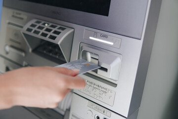 Close up picture of a person using ATM, inserting card to the machine before withdrawing money.