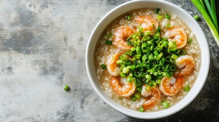 An overhead shot of a traditional shrimp rice porridge dish, showcasing plump shrimp, aromatic rice, and vibrant green onions in a delicate white bowl