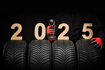 Winter car tires service and hands of mechanic with wheels screwdriver and text 2025 happy new year...