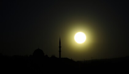 Silhouette of mosque at dawn with bright sun.