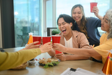 Group of colleagues laughing and clinking cups to celebrate at office party