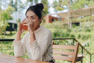 Fototapeta premium Beautiful young Asian woman is sitting outdoor while drinking morning coffee or tea.