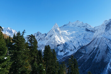 Fototapeta premium Picturesque landscape in Dombay with amazing snow-capped peaks and majestic blue slopes of North Caucasus Mountains. Mountain ski resort in Karachay-Cherkessia, Russia