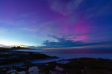 Silhouette of Dunstanburgh Castle with a spectacular Aurora above. Northumberland, England, UK.