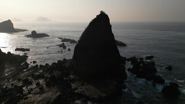Drone view of Papuma Beach at sunrise with waves and a rocky cliff in the water