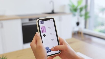 Caucasian woman browsing online store for clothing items using smartphone. Image depicts convenience of online shopping with focus on technology. Hands holding phone show webpage with clothes options.