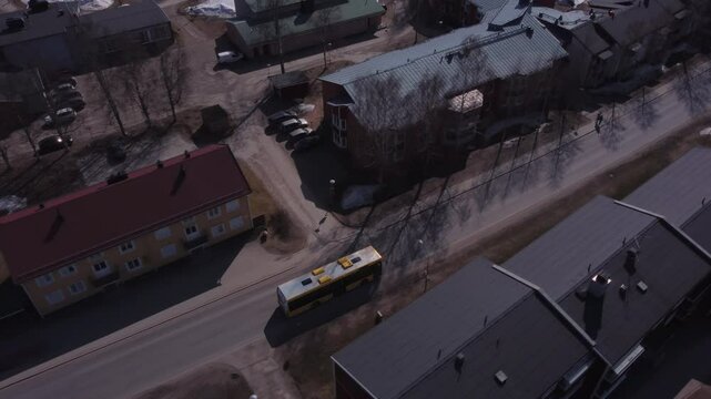 4K Aerial Tracking Shot of a Bus Driving Down the Street in a Small Suburb, Surrounded by Houses and Small Apartment Buildings.