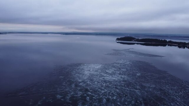 Aerial view of a thin ice layer floating on top of the water during a cloudy and misty morning