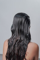 Back portrait of a young Asian woman with long hair, getting her hair washed using shampoo.