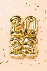 New year 2025 balloon celebration card. Gold foil helium balloons number 2025, party decoration, gold confetti stars on beige background. Flat lay, merry christmas banner, happy holidays concept.