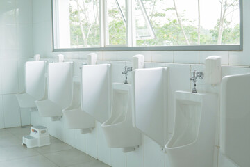 White urinals are lined up in a row in a public restroom with a partition between them.