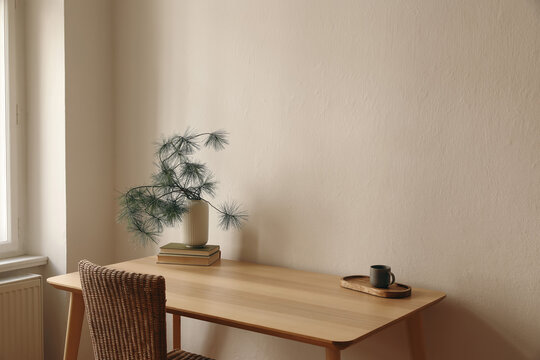 Scandinavian Christmas interior. Winter home decor. Cup of coffee, books on wooden table near window. Rattan chair. Pine tree branches in white vase. Beige wall background. Empty copy space.
