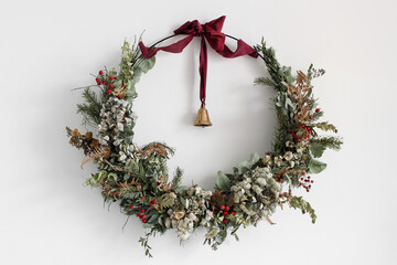 Beautiful huge advent wreath made of fir tree branches, red berries, dry flowers hanging on white...