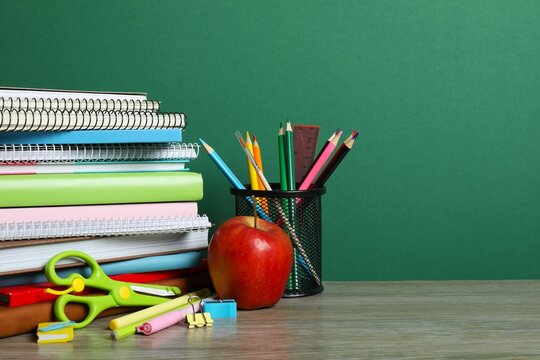 Back to school. Close-up of colorful stationery, textbooks, red apple on green chalkboard