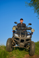 man sitting on a quad bike in nature, young guy riding a quad bike through the fields