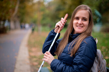 A visually impaired woman with a white cane sitting on a bench in a park on an autumn day