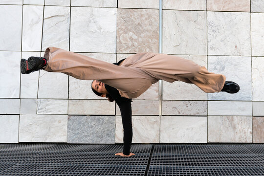 A young woman in tan pants and black t-shirt breakdancing performing a handstand on a metal grid