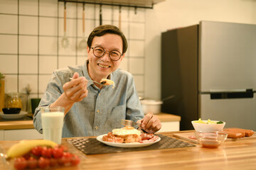 Middle aged man enjoying a hearty breakfast on wooden table in cozy home kitchen