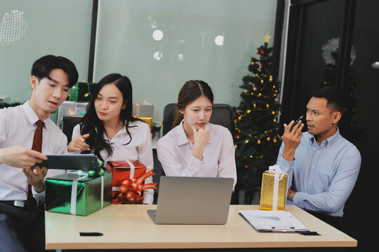 full length view of a group of business team wearing red Santa hat and exchange gift box together in the office for Christmas.