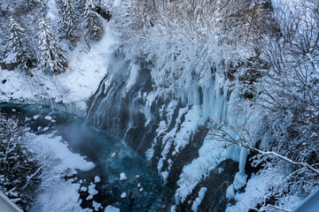 Stunning Winter Waterfall Surrounded by Ice and Snow in a Scenic Forest Landscape with Frozen Trees and Crystal Clear Water Flowing Beneath the Ice