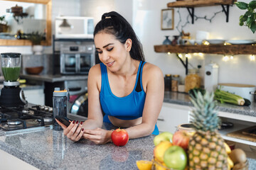 Latin woman in activewear using mobile phone in kitchen after fitness workout at home in Mexico Latin America, young hispanic fitness female	
