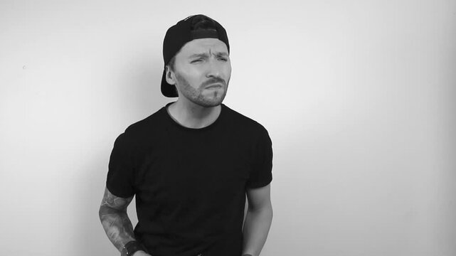 Black and white footage of a man with a full sleeve tattoo who can't see something and puts on glasses with a black frame. He begins to squint and move forward to see better, he sees and nods after.