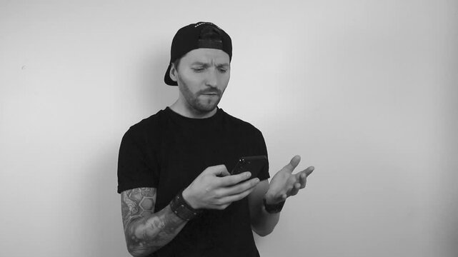 Grayscale footage of a man with black tattoo sleeve watching his phone, getting some bad news, reading something or watching and gets extremely angry. Man scream and yells at the phone, waving hands