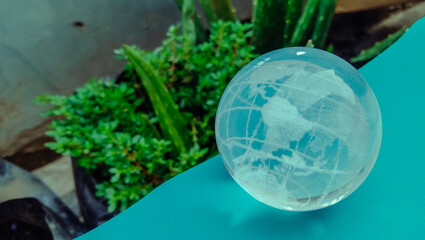 A transparent globe on a bright blue carpet in front of a potted plant. A concept to protect the earth and its inhabitants from global warming and other environmental issues.