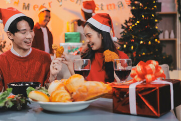Group of young Asian man and women as friends having fun at a New Year's celebration, holding gift boxes standing by Christmas tree decoration, midnight countdown Party at home with holiday season.