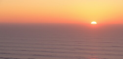 Obraz premium A breathtaking panoramic view of a golden sunset over a calm ocean, with soft waves reflecting hues of orange, pink, and purple