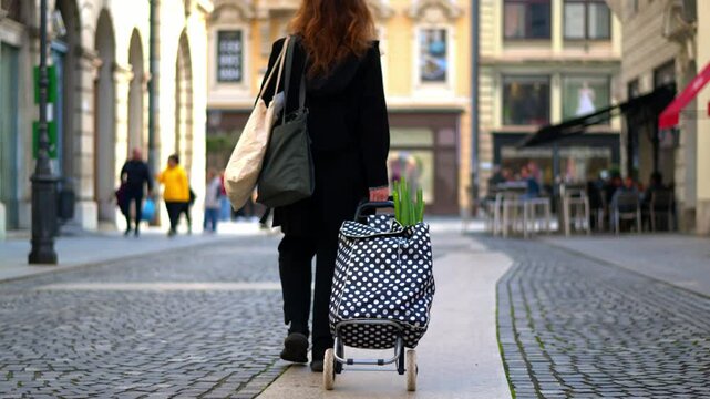 woman walking in a european classic street with a shopping trolley with reusable bags and some vegetbles visible, after shopping in the fresh market. Slow motion x2