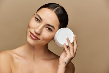 Young brunette applies skincare, smiling and exuding confidence and charm.