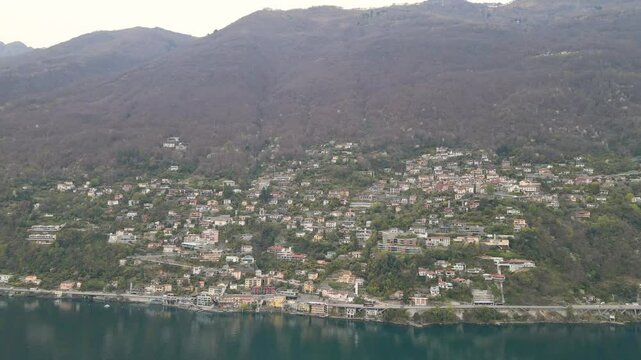 Capturing the charming town of Ronco sopra Ascona by lake Maggiore in Canton Ticino, Switzerland from above, featuring colorful buildings, lush greenery, and a serene lake surrounded by alps aerial