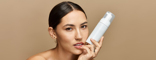 Young brunette woman highlights a skincare product while posing with confidence and elegance.