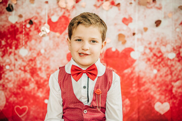 Smiling boy in red vest and bow tie with Valentine's heart backdrop
