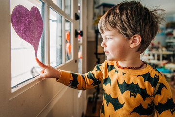 Toddler in bat-print pajamas points to a purple heart on a window