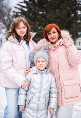 A mother and her two daughters, a teenager and a younger child, enjoy a snowy winter day together. They share laughter and warmth amidst the cold, surrounded by a beautiful, frosty landscape