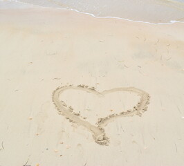 Heart shape in sand on gorgeous beach with wave on background.