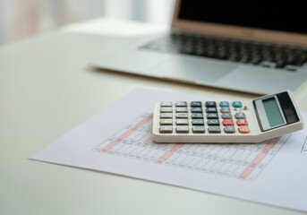 Calculator placed on financial statement with laptop in background suggesting accounting work