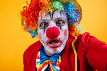 A pensive, sad adult clown on a vibrant yellow background.